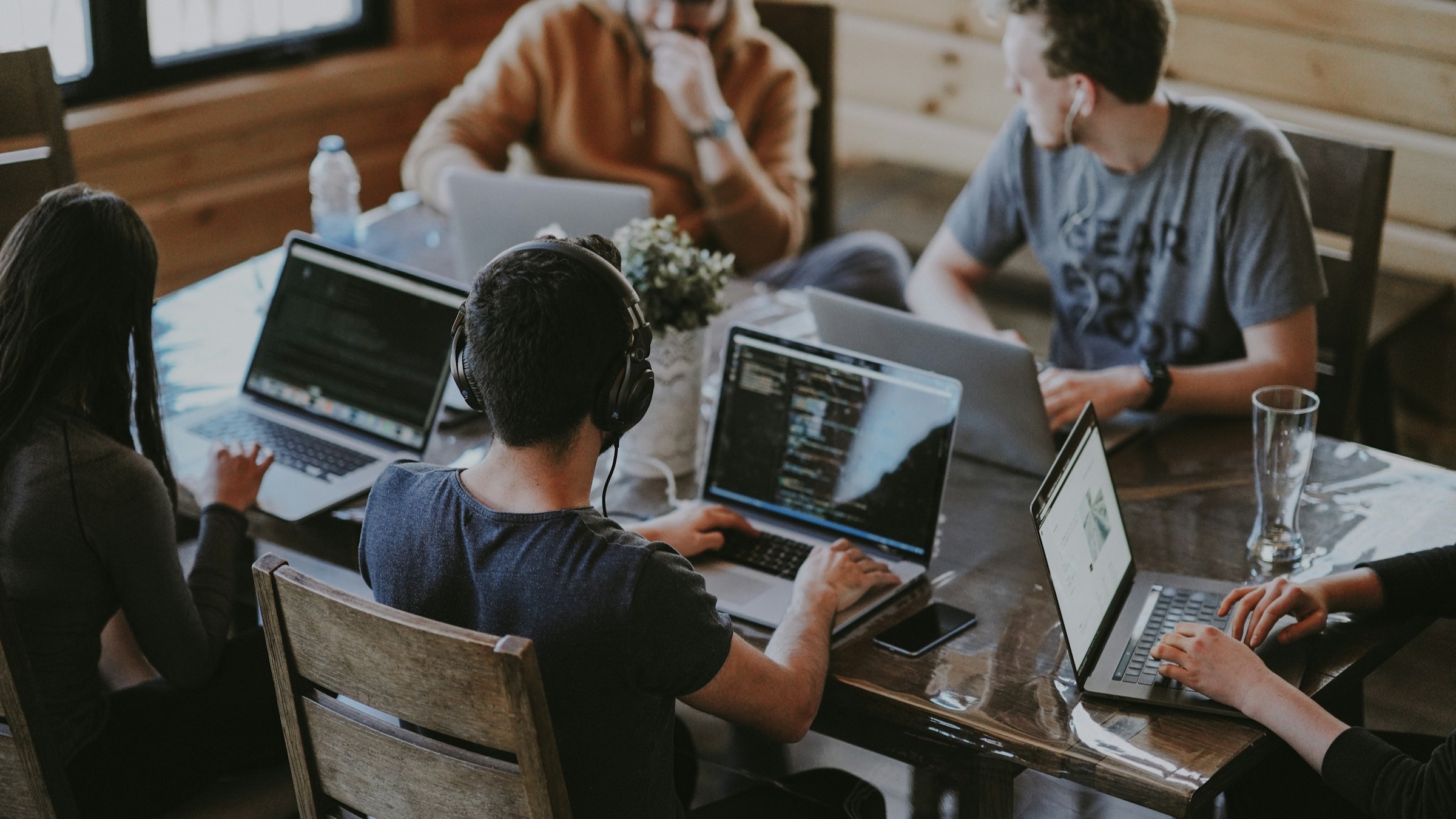 Un grupo trabaja en sus laptops alrededor de una mesa de madera, en una sala de oficina